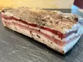 Ein Stück roher Pancetta mit deutlichen Schichten aus Fleisch und Fett, bestreut mit schwarzem Pfeffer. Perfekt, um ihn roh zu genießen.