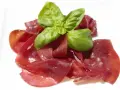Dünne Scheiben von Bresaola, einem luftgetrockneten Rindfleisch, garniert mit frischem Basilikum.