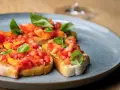 Drei Scheiben geröstetes Brot, belegt mit frischen Tomaten und Basilikum. Ein authentisches rezept bruschetta original italienisch.
