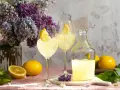 Erfrischender Limoncello Spritz mit Bitter Lemon, garniert mit Zitronenspalten, neben frischen Zitronen und einem üppigen Fliederstrauß.