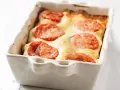 Gorgonzola Lasagne mit Tomaten und geschmolzenem Käse in einer weißen Auflaufform.