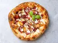 Eine köstliche Pizza aus Neapel mit Kartoffelscheiben, Speck, Nüssen und einem Hauch von Basilikum.
