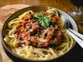 Herzhafte bolognese mit speck, serviert auf Bandnudeln, garniert mit Basilikum und Parmesan.