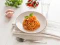 Ein Teller mit Linguini Nudeln mit Garnelen und Tomatensauce, garniert mit Petersilie. Daneben Schalotten, Chilis und ein Glas Wasser.