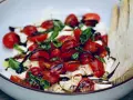 Burrata Caprese Salat mit Kirschtomaten, Basilikum und Balsamico-Dressing, serviert in einer Schüssel mit Holzsalatbesteck.