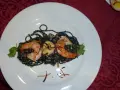 Schwarze Spaghetti mit Garnelen, garniert mit Koriander und knusprigen Zwiebeln. Ein köstliches Gericht, das auf einem weißen Teller serviert wird.