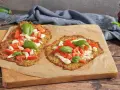 Zwei leckere Zucchini-Pizzen mit Mozzarella, Tomaten und Basilikum auf Backpapier.