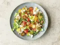 Bunter Tomatensalat mit cremiger Burrata, Rucola und Pinienkernen, garniert mit Basilikum.