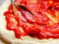Eine Löffelspitze verteilt die original italienische pizzasauce auf einem Pizzateig.
