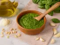 Frisches Pesto-Rezept original in einer Schale, umgeben von Basilikum, Pinienkernen, Knoblauch, Parmesan und Olivenöl.