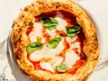Eine echte italienische Pizza Margherita mit geschmolzenem Mozzarella, Tomatensauce und frischem Basilikum auf einem Marmortisch.