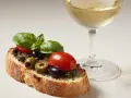 Bruschetta mit Olivencreme, Tomaten und Basilikum. Ein Glas Weißwein daneben. Perfekt für ein schnelles olivencreme rezept.