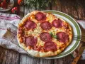 Eine köstliche Pizza Salami mit geschmolzenem Käse und frischem Basilikum auf einem rustikalen Holztisch.