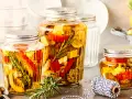 Drei Gläser mit italienischem Fingerfood: eingelegtes Gemüse wie Paprika und Zucchini mit Kräutern in Öl.
