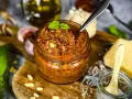 Ein Glas mit leuchtend rotem Pesto, garniert mit Basilikum. Daneben liegen Pinienkerne, Knoblauch und ein Stück Parmesan.