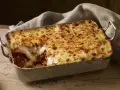 Herzhafte Lasagne mit goldbraun überbackener Käseschicht und einem Hauch von Creme Fraiche, serviert in einer Metallform auf Holztisch.
