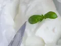 Cremiger Stracchino Käse mit Basilikum, bereit für ein köstliches Stracchino Rezept. Ein Messer liegt daneben.