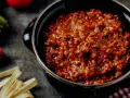 Herzhafte Bolognese-Sauce in einem Topf, daneben frische Bolognese-Zutaten wie Karotten, Sellerie und Tomaten.