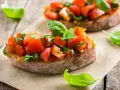 Zwei Bruschetta mit frischen Tomaten und Basilikum, garniert mit einem Hauch von Paprika, auf rustikalem Holz.