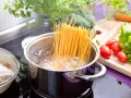 Spaghetti kochen in sprudelndem Wasser. Die richtige **Tagliatelle Kochzeit** ist entscheidend für ein perfektes Pastagericht. Frisches Gemüse wie Brokkoli, Karotten und Tomaten liegen bereit.