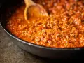 Ein Holzlöffel rührt in einer Pfanne mit köchelndem Sos bolognese.