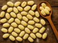 Frische Gnocchi Nudeln, liebevoll geformt und auf einem rustikalen Holztisch arrangiert, einige davon auf einem Holzlöffel.