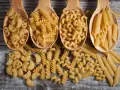 Vier Holzlöffel mit verschiedenen Nudelsorten: Maccheroni, Fusilli, Cavatappi und Penne. Die perfekte Menge Nudeln pro Person für ein köstliches Essen.