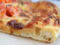 Ein Stück Pizza mit geschmolzenem Käse und Tomaten. Der Teig ist luftig und goldbraun gebacken, typisch für eine Pizza Sourdough.