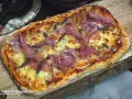 Eine rechteckige Pinsa mit geschmolzenem Käse und hauchdünnen Scheiben Schinken belegen. Köstlich!