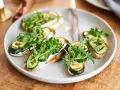 Italienische Crostini mit gegrillter Zucchini, Frischkäse und Rucola auf einem Teller.