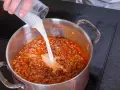 Milch wird in einen Topf mit köchelnder Bolognese gegossen, um die Sauce cremiger zu machen.