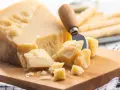 Ein Stück Parmesan mit grob abgebrochenen Stücken und einem Käsemesser. Die Parmesan Rinde ist sichtbar.
