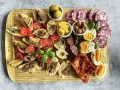 Kaltes italienisches Fingerfood: Bruschetta mit Sardellen, Tomaten, Oliven, Käse, Eiern und Salami auf Holzbrett.