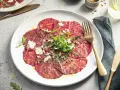 Carpaccio selber machen: hauchdünne Rinderfiletscheiben mit Rucola, Parmesan und Pinienkernen auf einem Teller.