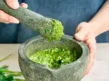Frische Kräuter werden im Mörser zermahlen, um zu zeigen, wie man Pesto zubereitet.