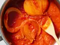 Tomatensoße mit Zwiebelstücken in einem Topf, bereit für Marcella Hazan Rezepte. Ein Holzlöffel rührt die köstliche Soße.