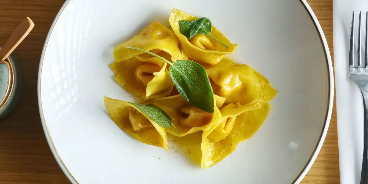 Gelbe Ravioli mit Salbeiblättern auf einem weißen Teller. Ein köstliches Gericht, das zeigt, was ist Ravioli: gefüllte Teigtaschen.