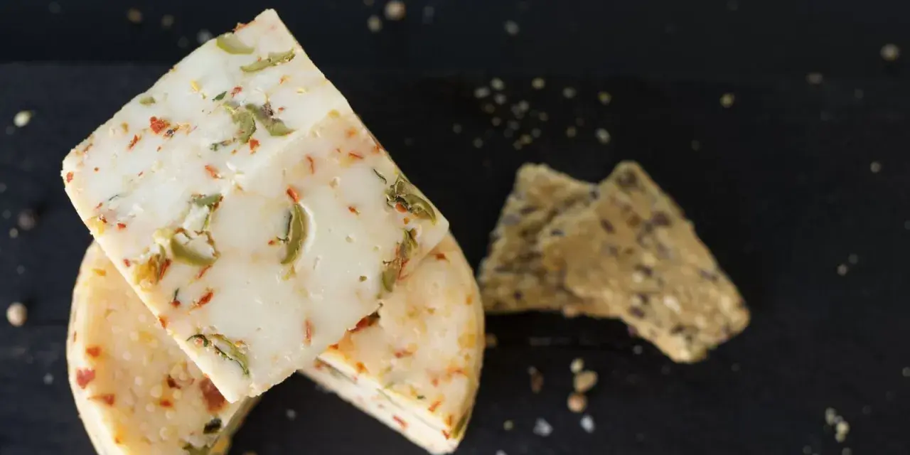 Käse mit Kräutern und Paprika, eine köstliche pecorino alternative, neben knusprigen Crackern auf dunklem Untergrund.
