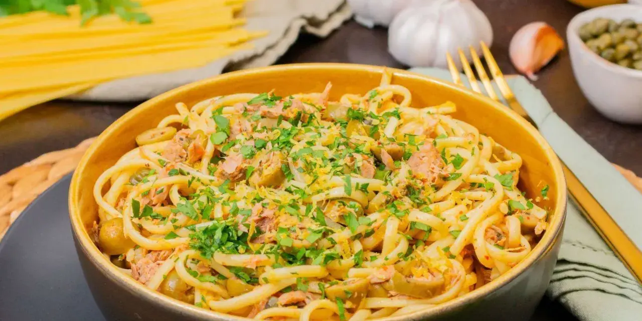 Eine Schüssel mit Thunfisch Pasta, garniert mit Petersilie und Zitronenschale. Oliven und Kapern sind ebenfalls sichtbar.