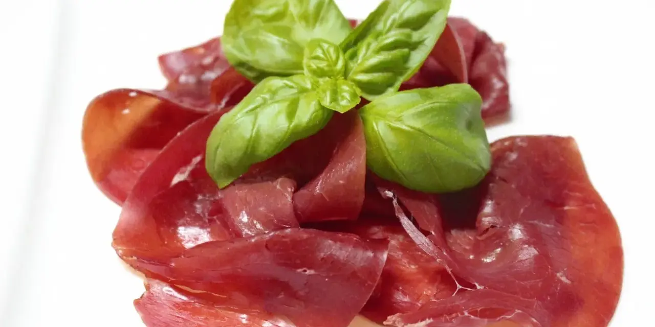 Dünne Scheiben von Bresaola, einem luftgetrockneten Rindfleisch, garniert mit frischem Basilikum.