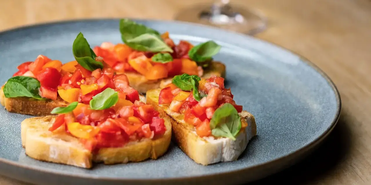 Drei Scheiben geröstetes Brot, belegt mit frischen Tomaten und Basilikum. Ein authentisches rezept bruschetta original italienisch.