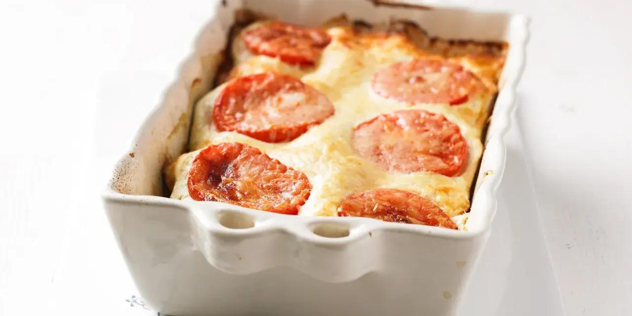 Gorgonzola Lasagne mit Tomaten und geschmolzenem Käse in einer weißen Auflaufform.