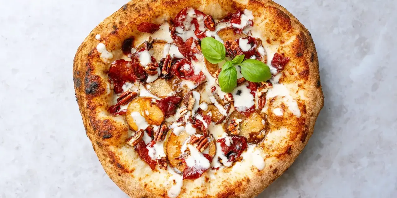 Eine köstliche Pizza aus Neapel mit Kartoffelscheiben, Speck, Nüssen und einem Hauch von Basilikum.