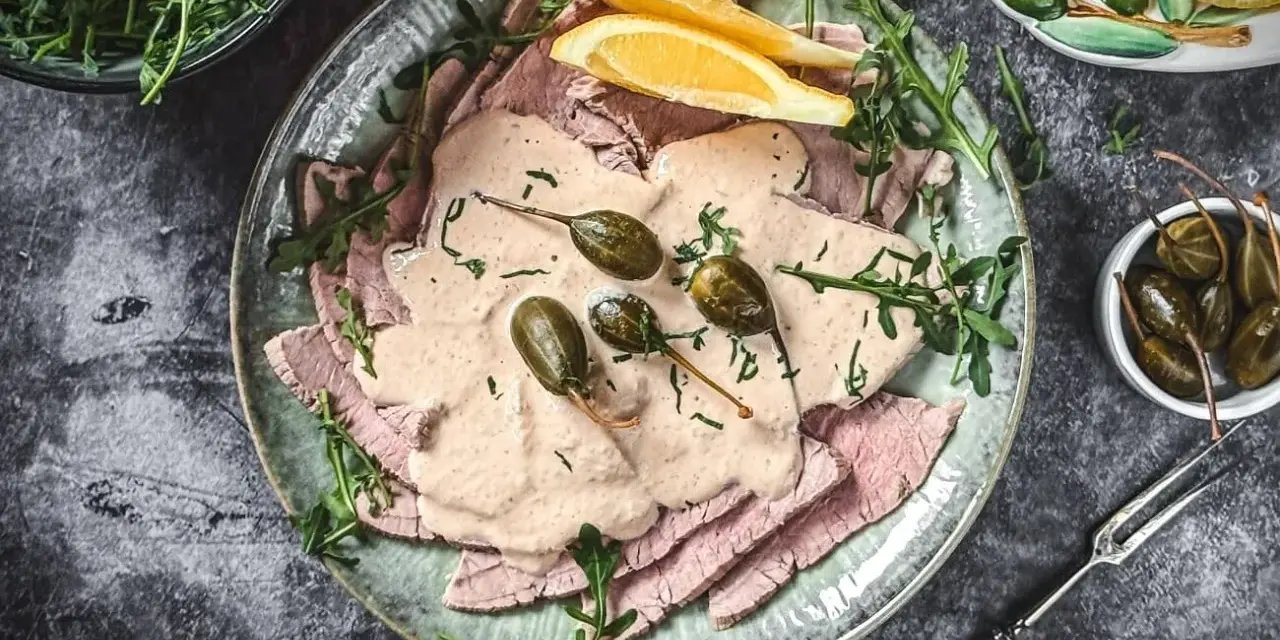 Vitello Tonnato Rezept Original Italienisch: Dünne Kalbfleischscheiben mit cremiger Thunfischsauce, Kapern und Zitronenspalten auf einem Teller.