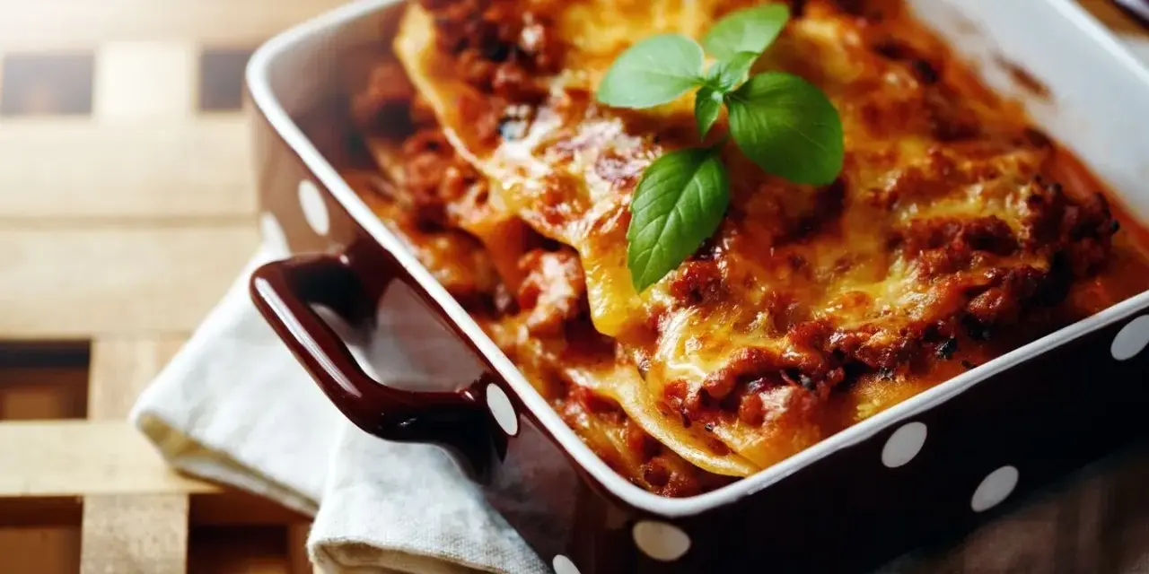 Herzhafte Lasagne Bolognese, eine der beliebtesten Lasagne Arten, dampft in einer braunen Auflaufform mit weißen Punkten. Frisch garniert mit Basilikum.