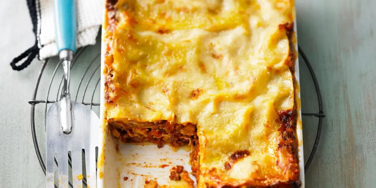 Eine goldbraun überbackene Lasagne mit einer cremigen Käseschicht. Ein Stück ist bereits entnommen, was die saftige Füllung offenbart. Diese Pistazien Lasagne sieht köstlich aus!