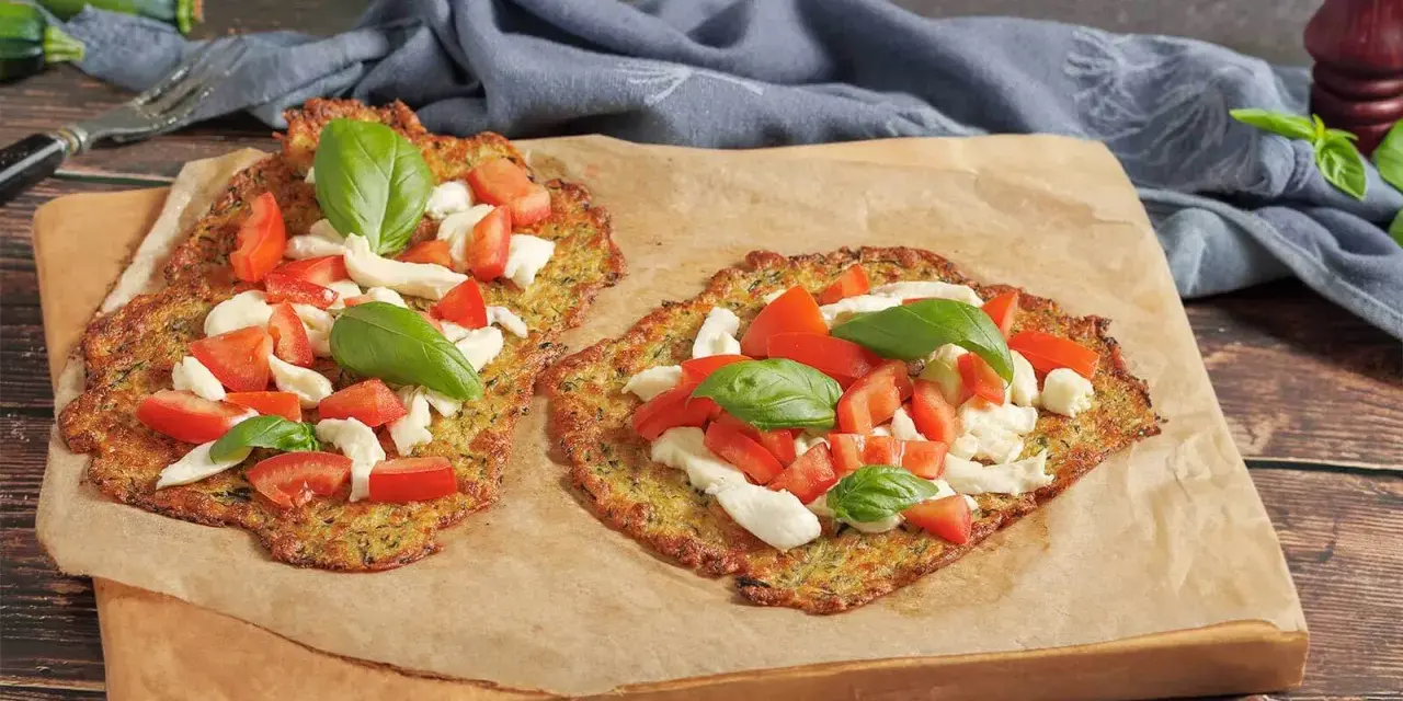 Zwei leckere Zucchini-Pizzen mit Mozzarella, Tomaten und Basilikum auf Backpapier.