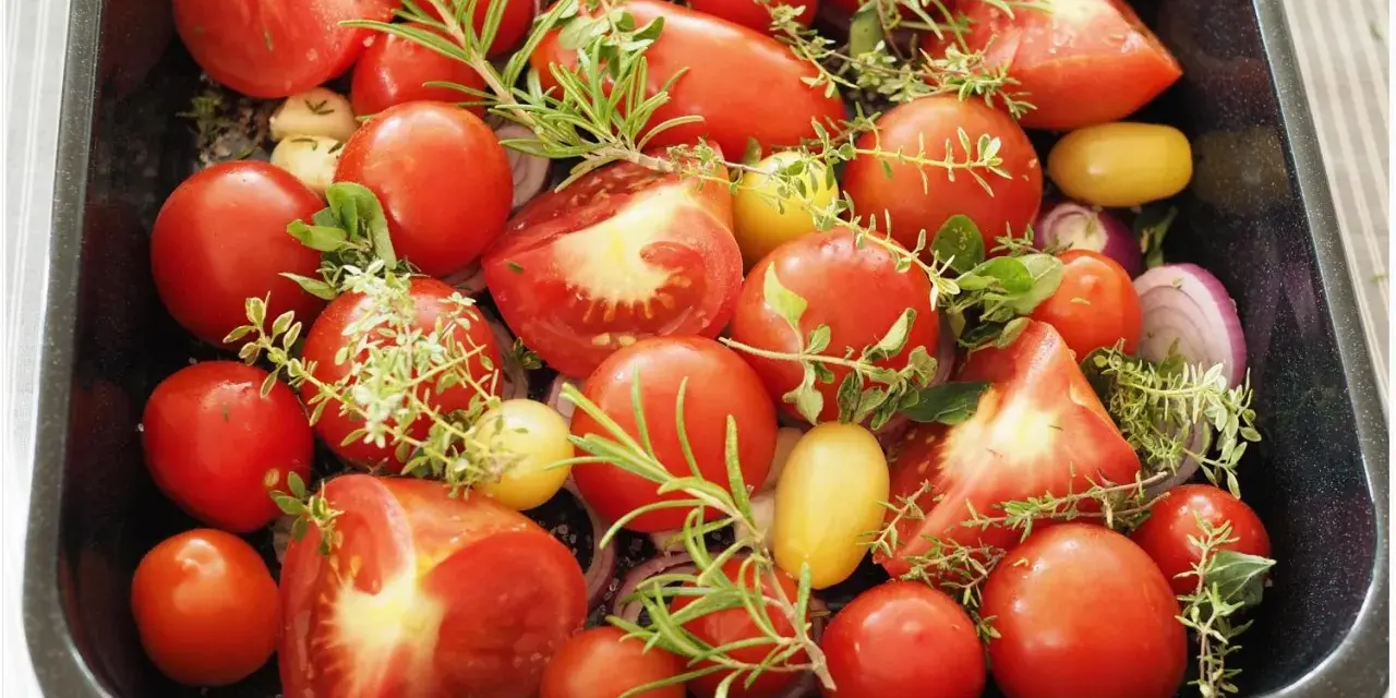Tomaten einkochen im Backofen: Frische Tomaten, Zwiebeln und Kräuter in einer Auflaufform, bereit für den Ofen.