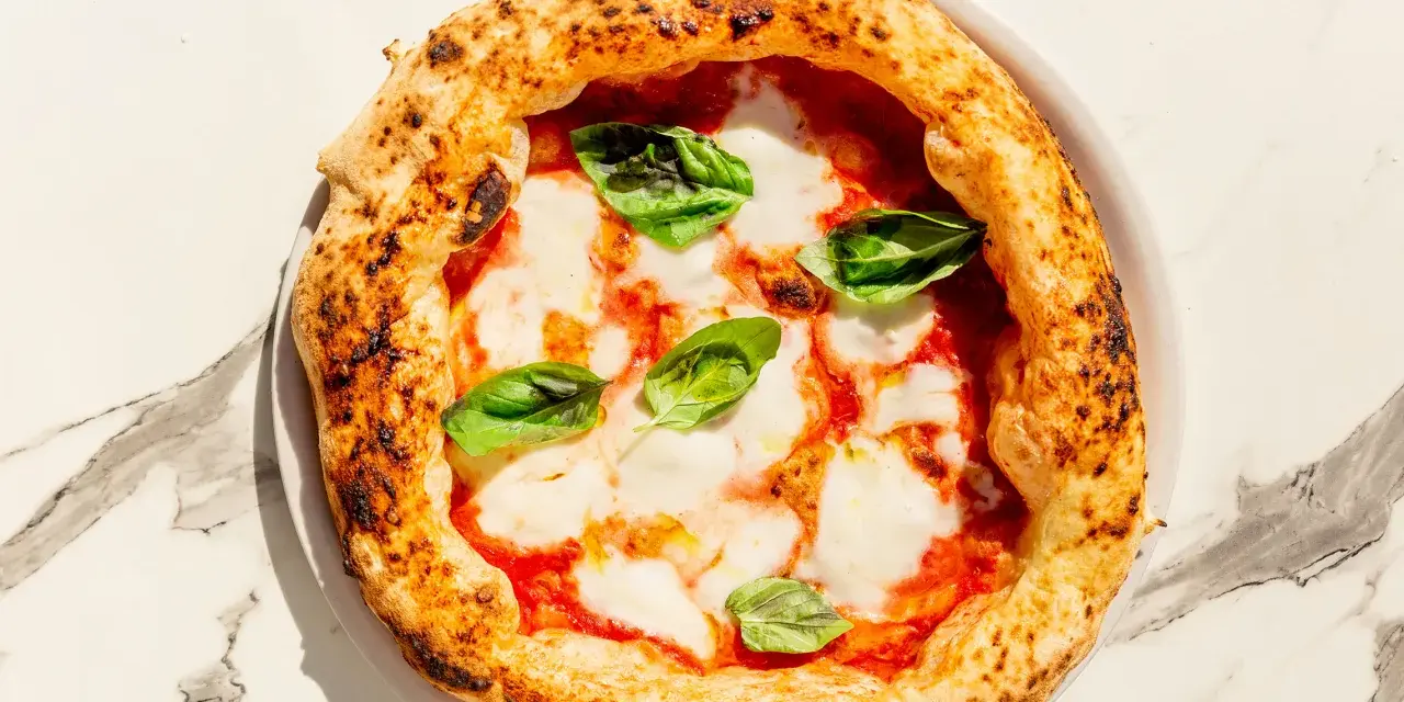 Eine echte italienische Pizza Margherita mit geschmolzenem Mozzarella, Tomatensauce und frischem Basilikum auf einem Marmortisch.