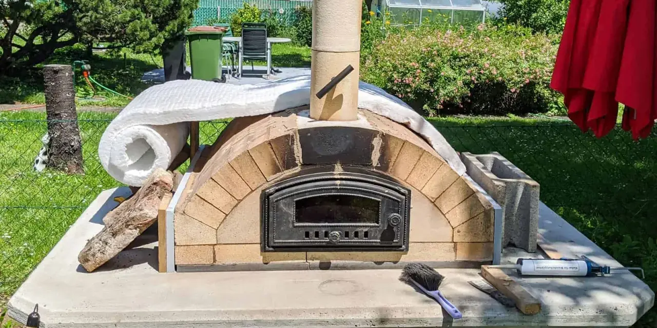 Ein selbstgebauter Pizzaofen im Garten, noch in der Bauphase, mit Isolierung und Schornstein. Bald bereit für die erste Pizza!